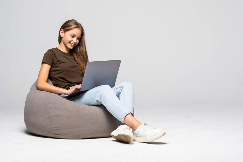 Mulher jovem com um computador no colo enquanto digita. Através de uma boa estratégia é possível reverter a base fraca nos estudos para a Residência Médica.